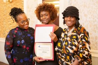 A student takes a photo holding up her scholarship alongside her mother on the right and one of the mother's colleagues during the UFT African Heritage Committee Dinner Dance on Feb. 7, 2025.