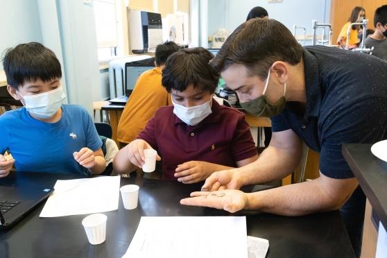 Jon Carrai, a history teacher at IS 187 in Brooklyn, examines the symbols on ancient Roman coins with two of his 6th-graders. 